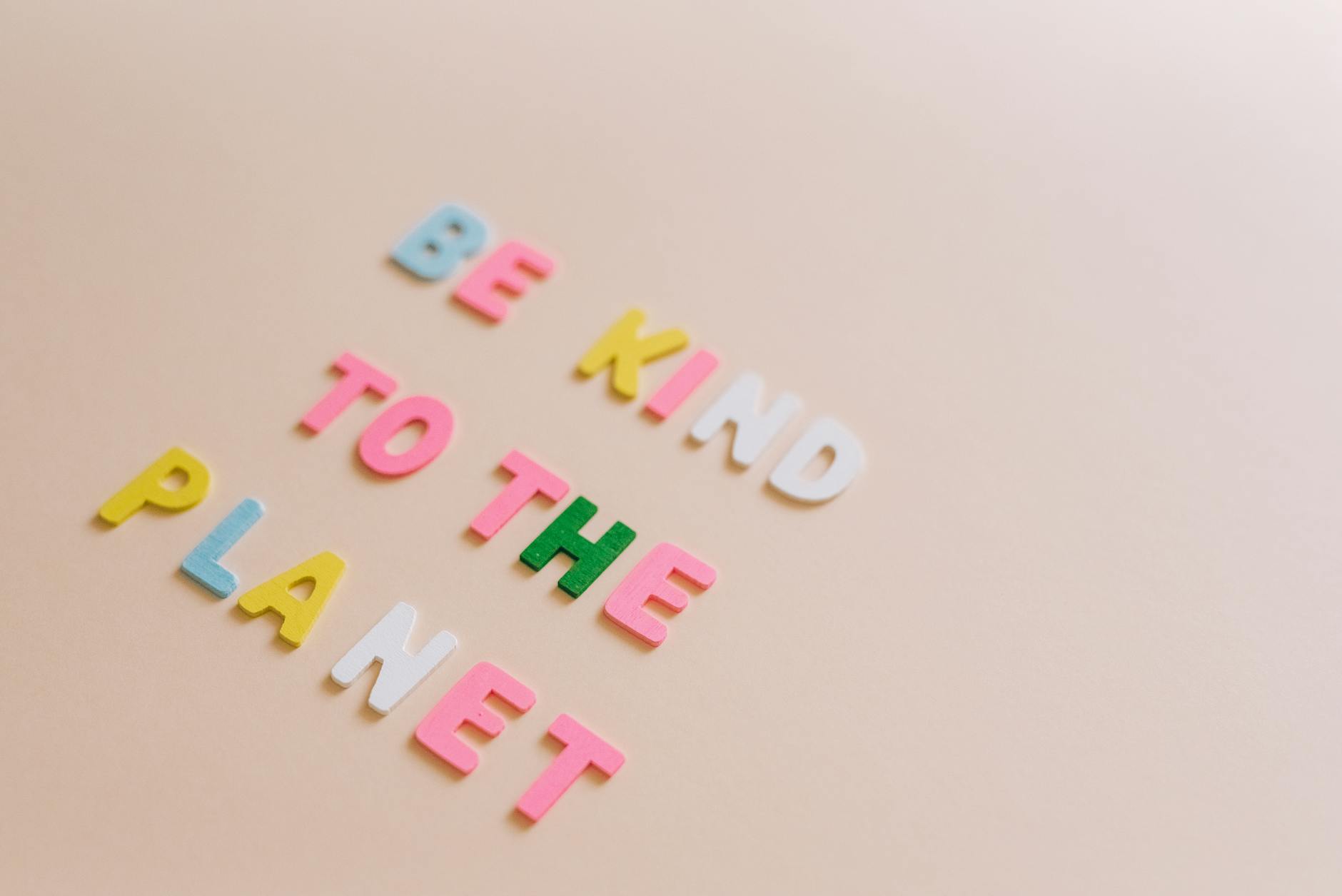 Kolorowe literki na beżowym tle tworzą napis Be Kind to the Planet