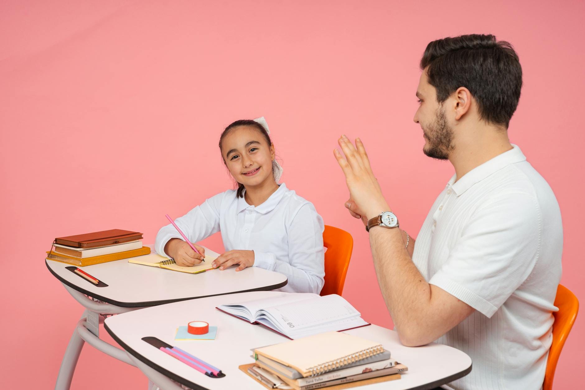 Nauczycielka tłumaczy zagadnienie uczennicy na tle różowej ściany