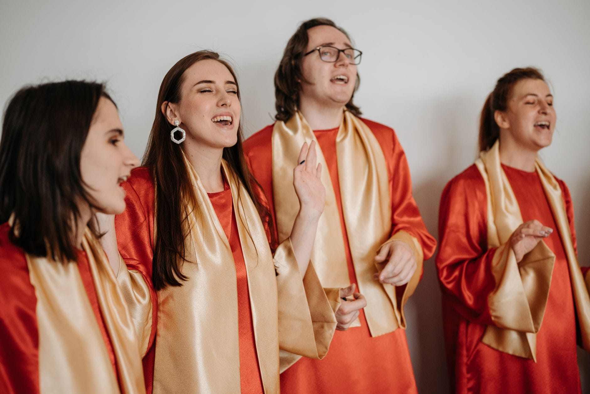 Chór dorosłych w czerwonych szatach liturgicznych śpiewa radośnie
