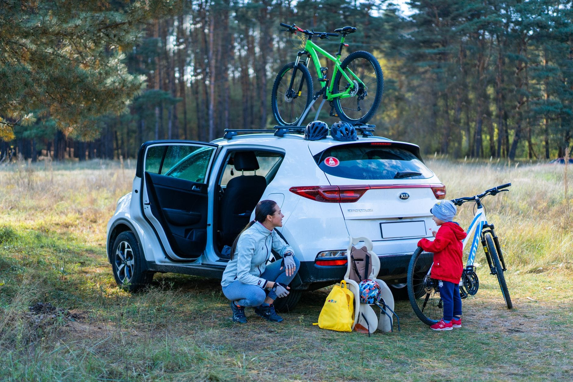 Mama z dzieckiem szykują rowery obok zaparkowanego auta w parku