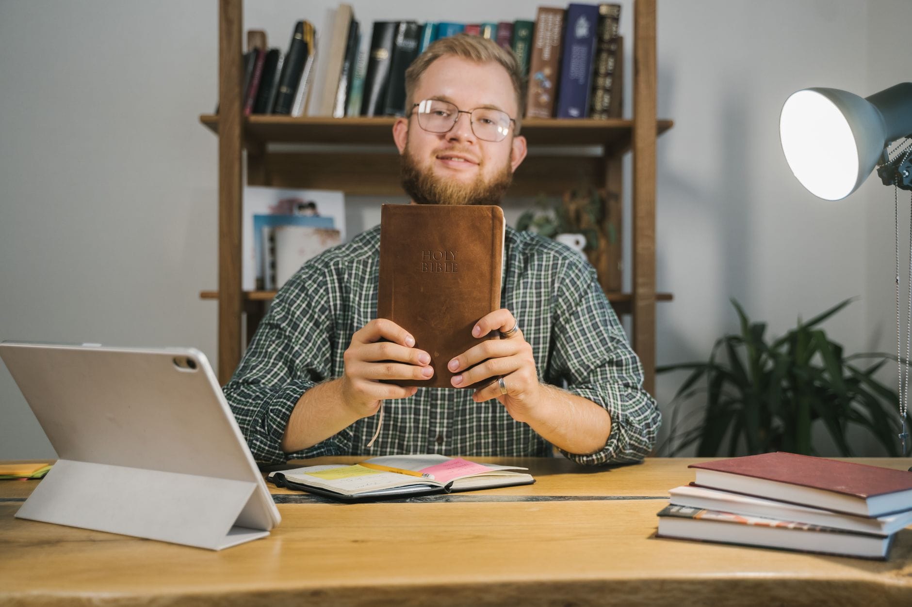 Mężczyzna w okularach trzyma Biblię przy biurku w pokoju pełnym książek