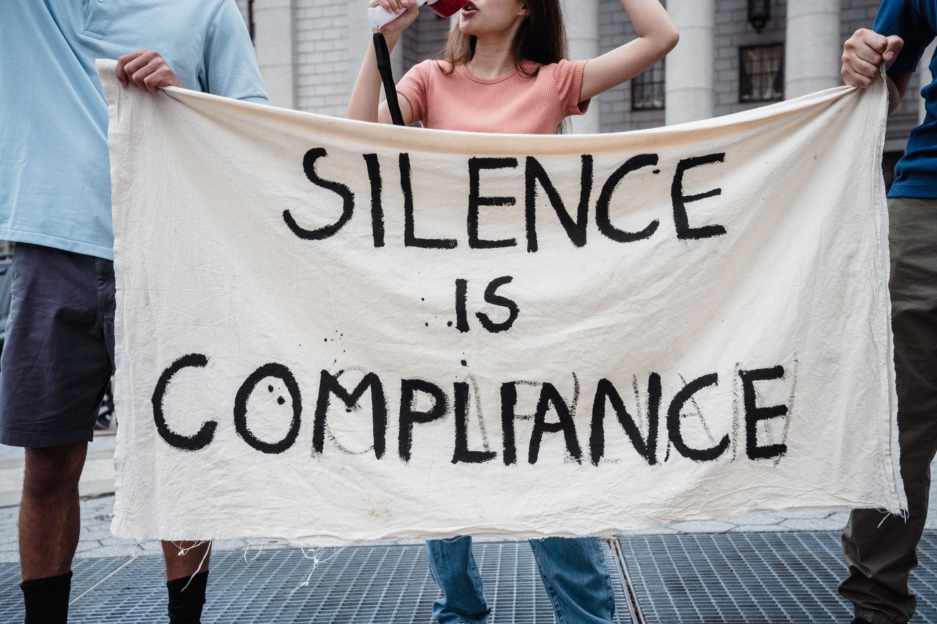 Demonstranci z transparentem Silence is Compliance podczas protestu na ulicy