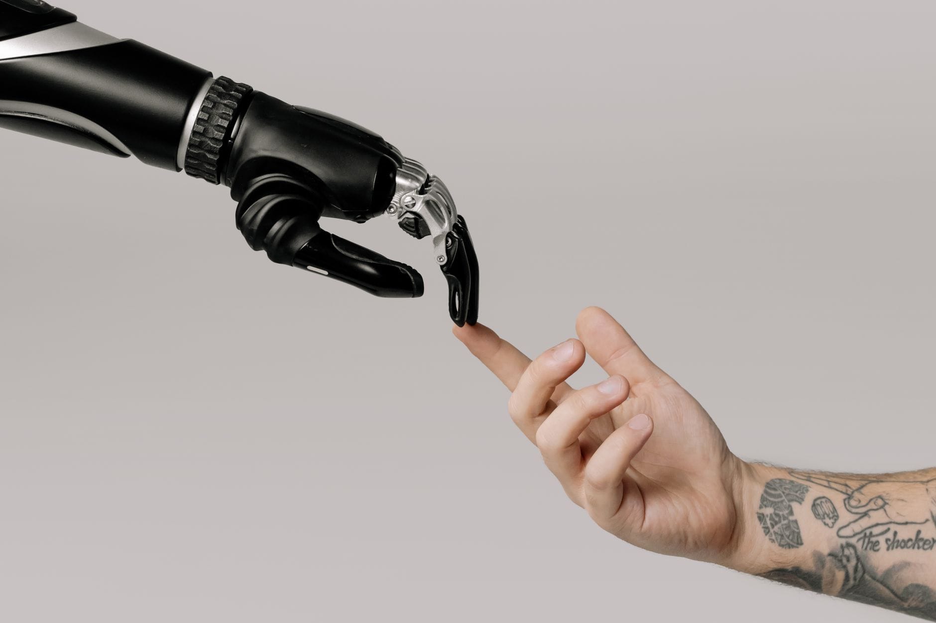 Wytatuowana dłoń człowieka wyciągnięta ku dłoni robota Wytatuowana dłoń człowieka wyciągnięta ku dłoni robota